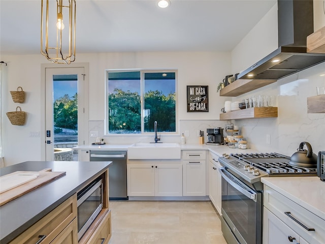 kitchen featuring white cabinets, appliances with stainless steel finishes, decorative light fixtures, sink, and range hood