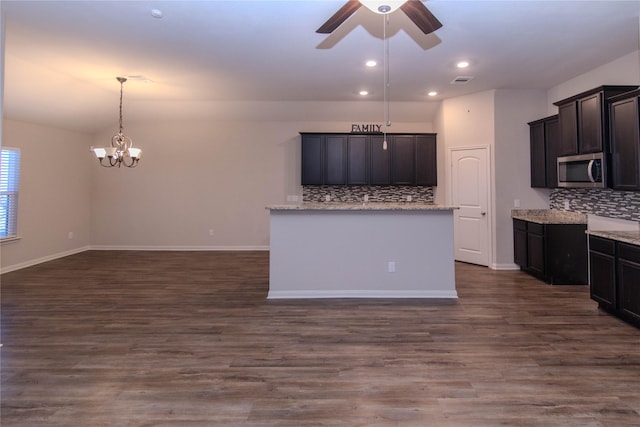 kitchen with decorative backsplash, hanging light fixtures, light stone countertops, dark hardwood / wood-style flooring, and ceiling fan with notable chandelier