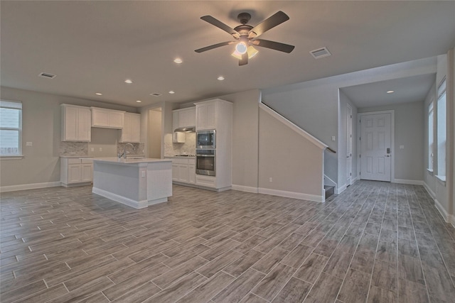 kitchen with white cabinets, built in microwave, oven, and a center island with sink