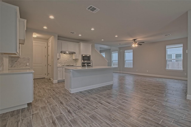 kitchen with ceiling fan, white cabinetry, stainless steel appliances, and an island with sink