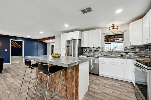 kitchen featuring appliances with stainless steel finishes, a breakfast bar area, recessed lighting, decorative backsplash, and visible vents