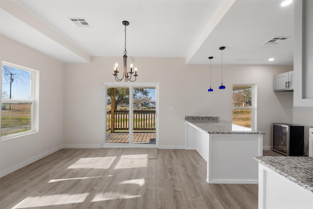 unfurnished dining area with light wood-type flooring, an inviting chandelier, beverage cooler, and plenty of natural light