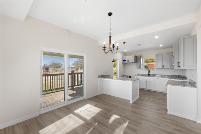 kitchen with an inviting chandelier, plenty of natural light, wood-type flooring, light stone counters, and sink