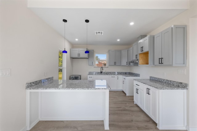 kitchen with pendant lighting, kitchen peninsula, sink, light wood-type flooring, and light stone countertops