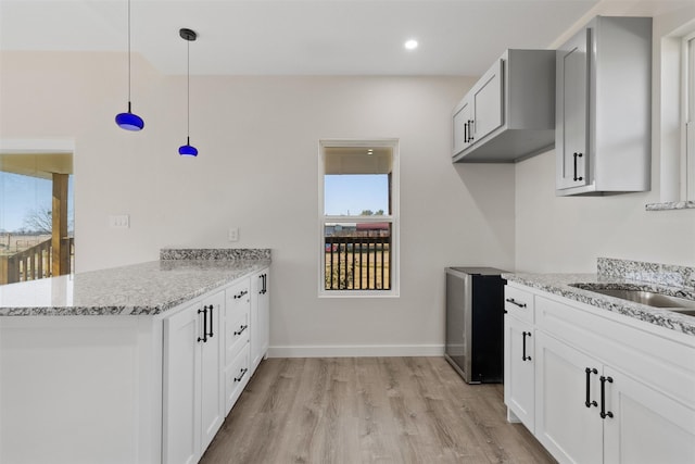 kitchen with light hardwood / wood-style floors, kitchen peninsula, hanging light fixtures, light stone countertops, and white cabinets