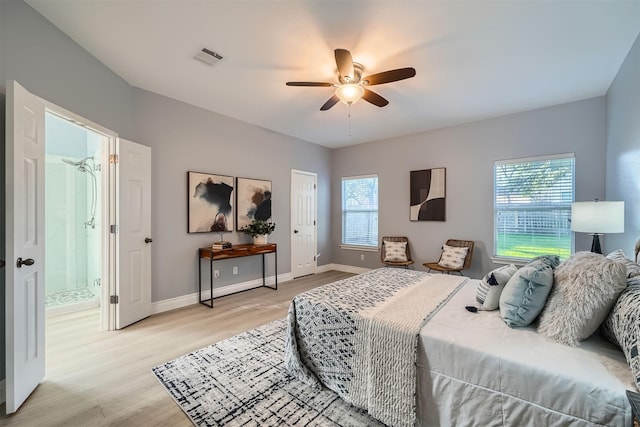 bedroom featuring ceiling fan, ensuite bath, light wood-type flooring, and multiple windows