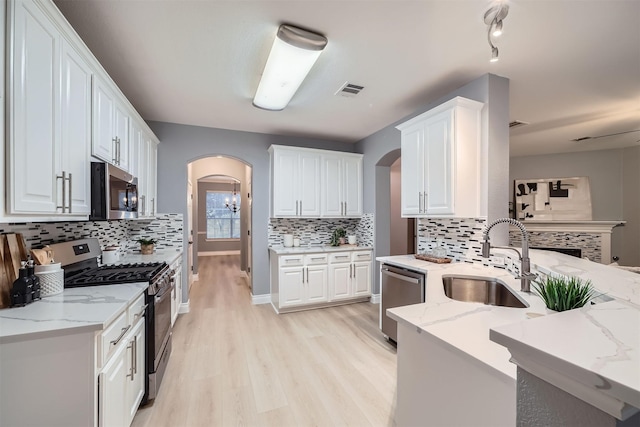 kitchen featuring stainless steel appliances, light wood-type flooring, white cabinets, light stone counters, and sink