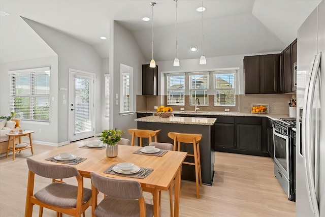 kitchen featuring lofted ceiling, a kitchen island, hanging light fixtures, light stone countertops, and stainless steel appliances