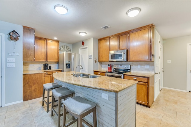 kitchen with light stone countertops, appliances with stainless steel finishes, an island with sink, and sink