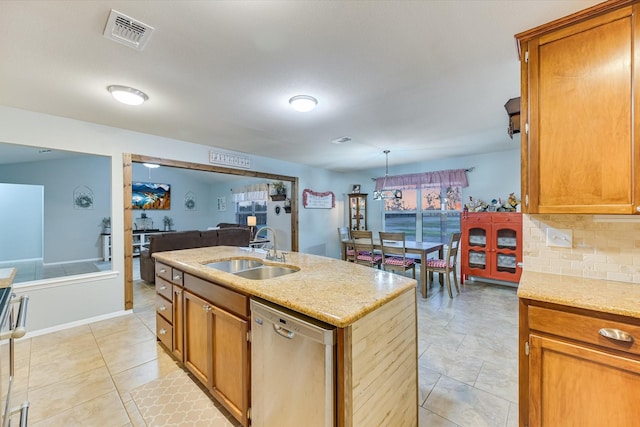 kitchen featuring dishwasher, decorative backsplash, sink, light stone countertops, and an island with sink