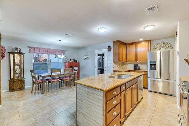 kitchen with pendant lighting, sink, a kitchen island with sink, light stone countertops, and stainless steel appliances