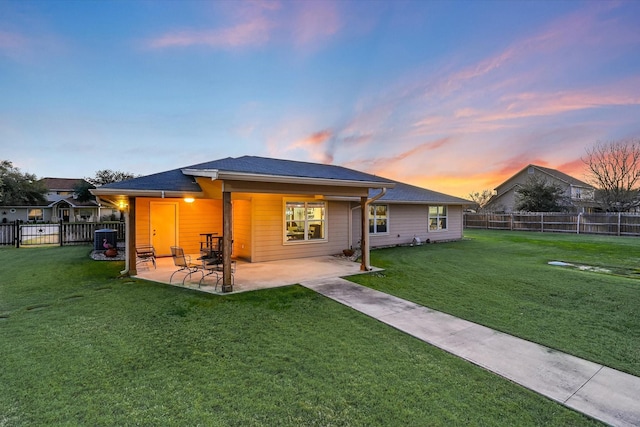 back house at dusk with a lawn and a patio area