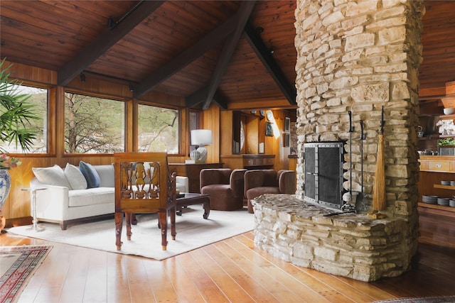 unfurnished living room with beam ceiling, a stone fireplace, wood ceiling, and wooden walls