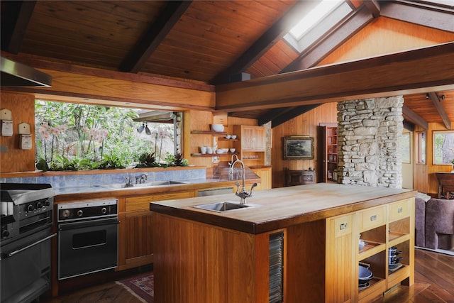 kitchen featuring wood walls, sink, a kitchen island with sink, wall oven, and wood counters