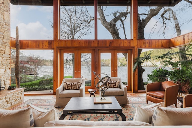 living room featuring a water view, a high ceiling, french doors, and wood walls