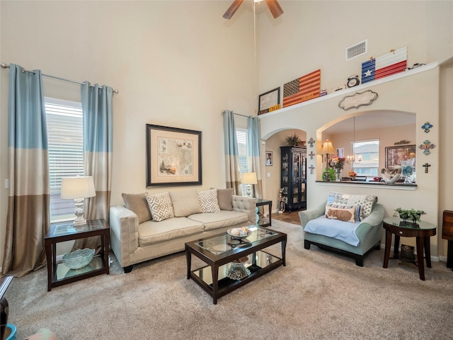 carpeted living room with plenty of natural light, ceiling fan with notable chandelier, and a high ceiling