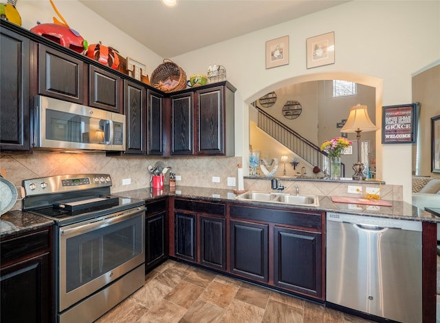 kitchen featuring kitchen peninsula, stainless steel appliances, dark stone counters, dark brown cabinetry, and sink