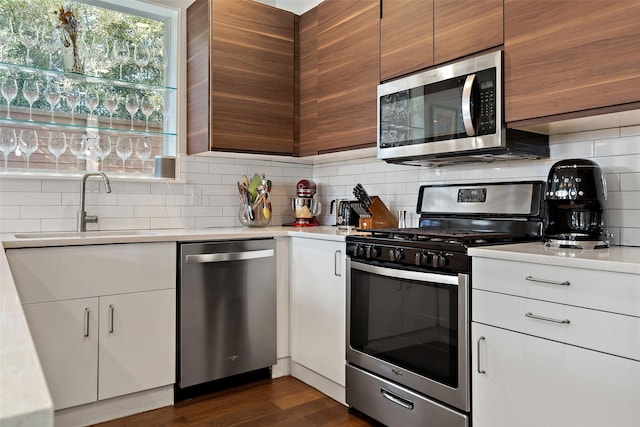 kitchen featuring appliances with stainless steel finishes, white cabinetry, dark hardwood / wood-style flooring, tasteful backsplash, and sink