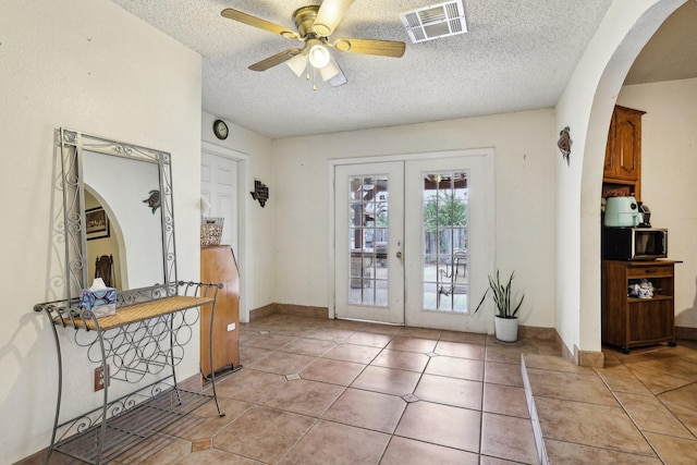 foyer entrance featuring ceiling fan, light tile patterned floors, french doors, and a textured ceiling