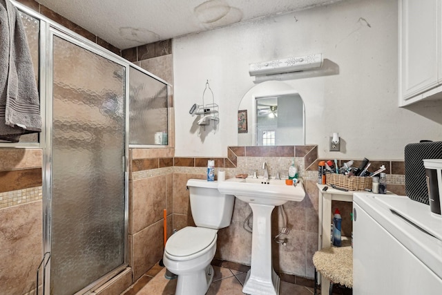 bathroom featuring toilet, a shower with shower door, tile walls, tile patterned floors, and a textured ceiling