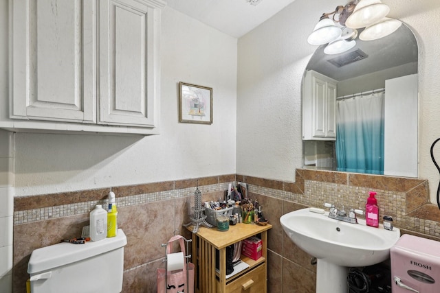 bathroom featuring toilet, tile walls, and sink