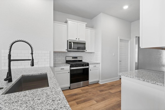 kitchen featuring light stone countertops, stainless steel appliances, white cabinets, and sink