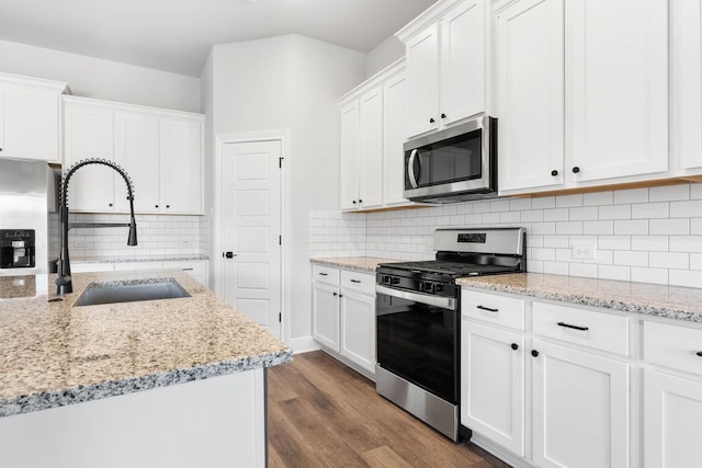 kitchen with white cabinetry, stainless steel appliances, sink, hardwood / wood-style flooring, and light stone counters