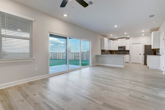 kitchen with light hardwood / wood-style floors, kitchen peninsula, ceiling fan, appliances with stainless steel finishes, and white cabinets