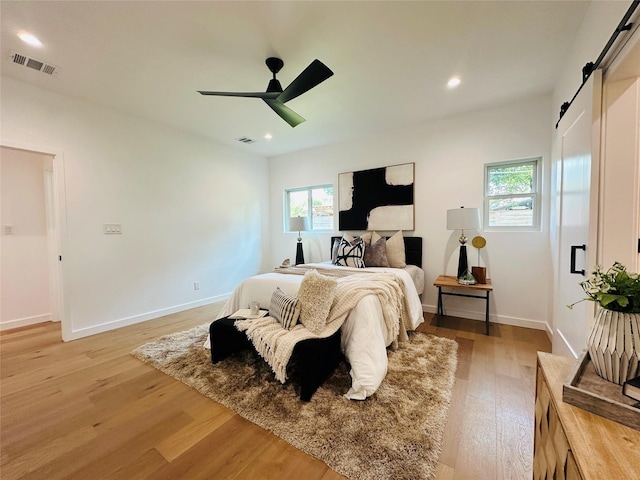 bedroom featuring ceiling fan, multiple windows, light hardwood / wood-style flooring, and a barn door