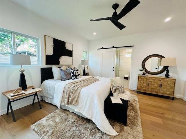 bedroom featuring ceiling fan, connected bathroom, wood-type flooring, and a barn door