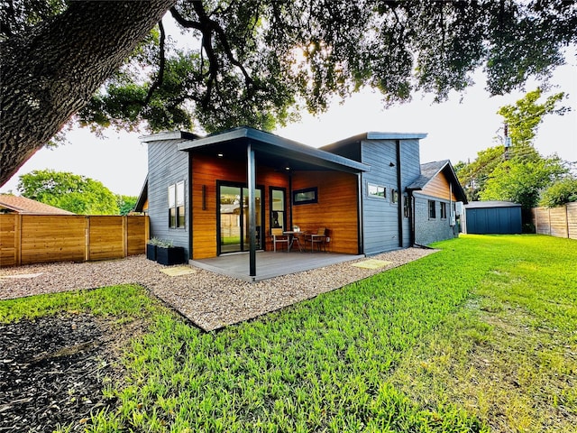 rear view of property featuring a patio area, a lawn, and a storage unit