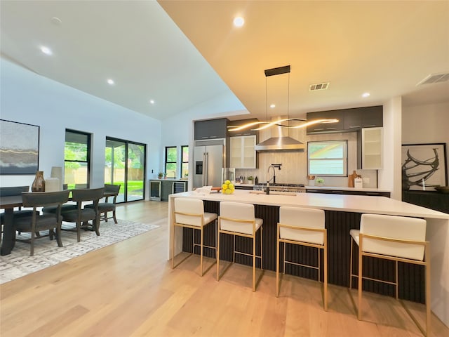 kitchen featuring a breakfast bar, wall chimney exhaust hood, stainless steel built in refrigerator, and light hardwood / wood-style flooring