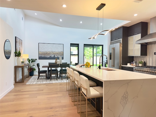 kitchen featuring built in fridge, decorative light fixtures, an island with sink, light hardwood / wood-style floors, and decorative backsplash