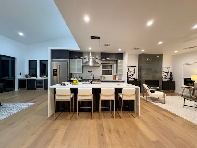 kitchen featuring built in fridge, backsplash, light hardwood / wood-style flooring, and an island with sink