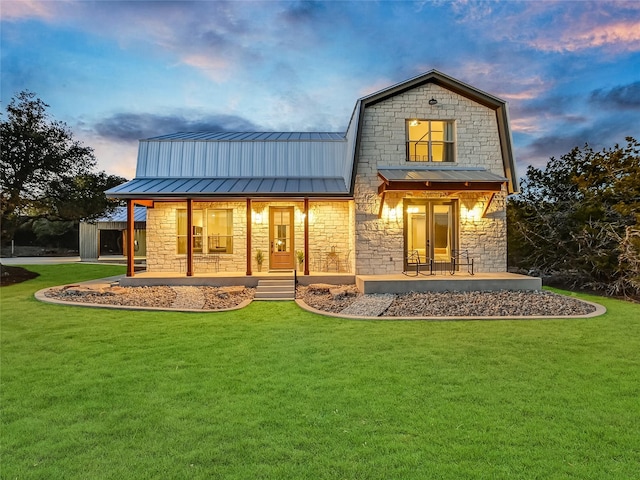 back house at dusk with a lawn and covered porch