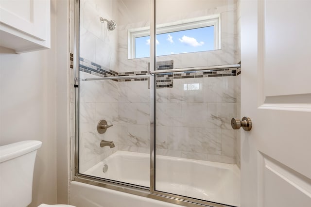 bathroom with toilet and shower / bath combination with glass door