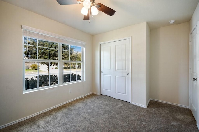 unfurnished bedroom with ceiling fan, a closet, and dark colored carpet