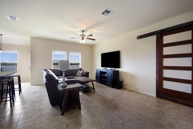 living room featuring ceiling fan, a barn door, and tile patterned flooring