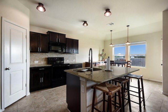 kitchen with decorative light fixtures, a kitchen island with sink, dark stone counters, black appliances, and sink