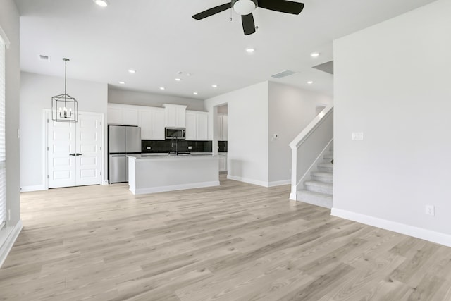 kitchen with a center island with sink, stainless steel appliances, hanging light fixtures, ceiling fan with notable chandelier, and white cabinets