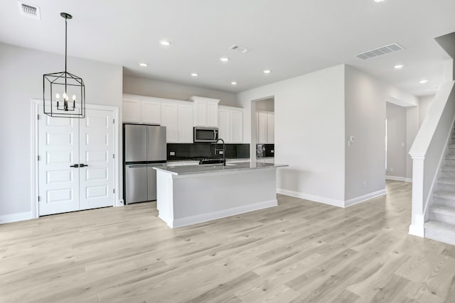 kitchen with backsplash, light hardwood / wood-style floors, a kitchen island with sink, appliances with stainless steel finishes, and white cabinets