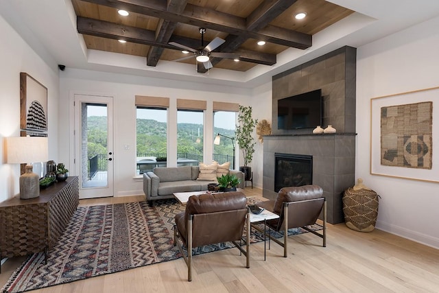 living room featuring ceiling fan, a tile fireplace, beam ceiling, coffered ceiling, and light wood-type flooring