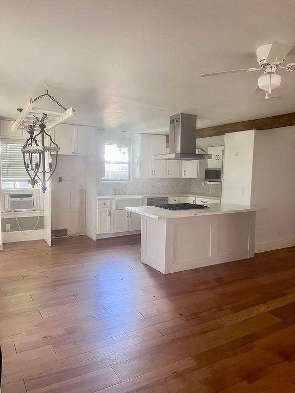 kitchen featuring white cabinetry, island range hood, kitchen peninsula, appliances with stainless steel finishes, and light wood-type flooring