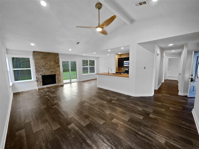 unfurnished living room featuring ceiling fan, a fireplace, dark hardwood / wood-style flooring, and lofted ceiling with beams