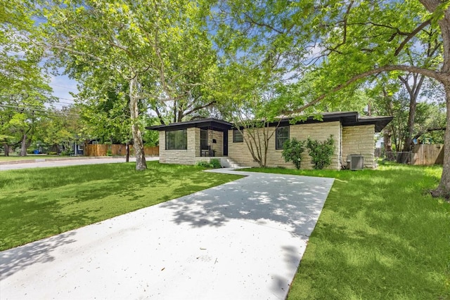 mid-century home with fence, central AC, a front lawn, and stone siding