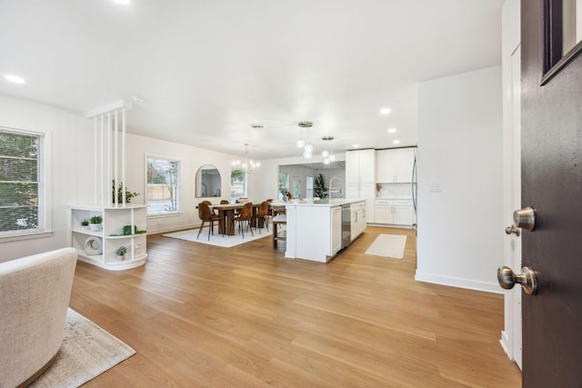 kitchen with stainless steel dishwasher, white cabinetry, an inviting chandelier, and light wood-type flooring