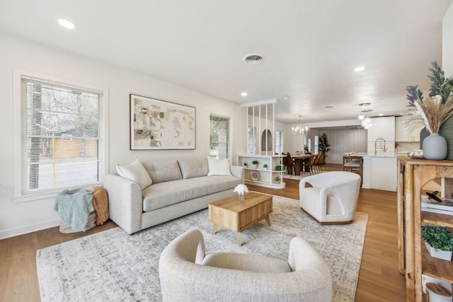 living room with an inviting chandelier, plenty of natural light, wood finished floors, and visible vents
