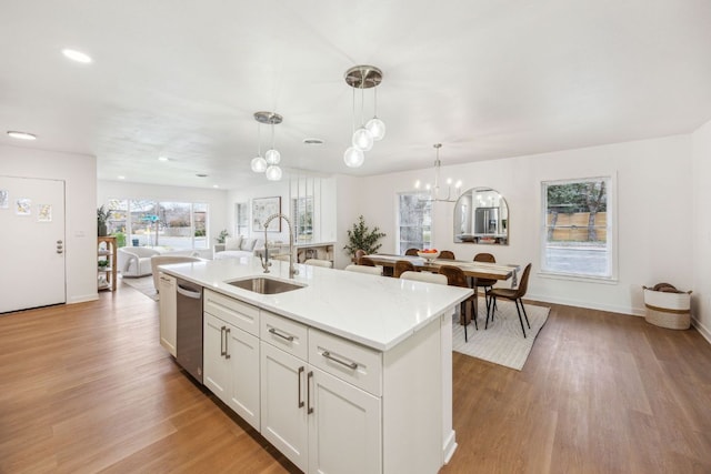 kitchen featuring a kitchen island with sink, dishwasher, a sink, open floor plan, and light wood-style flooring
