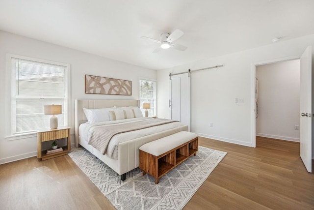 bedroom with baseboards, a barn door, a ceiling fan, and wood finished floors