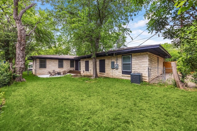 rear view of property featuring a lawn, a patio area, central AC, fence, and stone siding